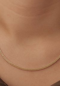 Collier en or avec des maillons entrelacés, texture lisse, repose contre le teint de la peau. Design simple avec un look classique et discret.