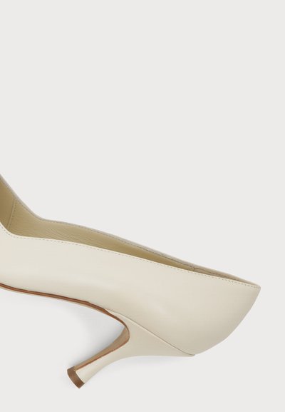 Chaussure à talon haut pour femme en cuir crème avec un bout pointu et un talon mince, incurvé et de hauteur moyenne, présentée sur fond blanc.