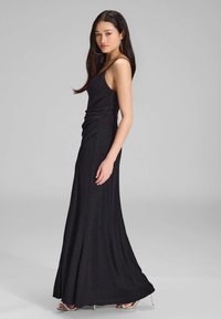 Mustakalla, hihaton iltapuku, jossa on tiivis yläosa ja laskostettu sivuyksityiskohta, virtaamassa liehuvaan hameeseen, valmistettu hohtavasta kankaasta.