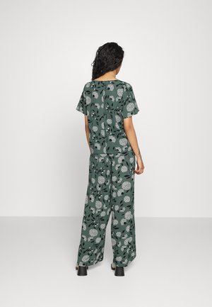 Grünes Blumenmuster, Kurzarm-Oberteil und weite Hose aus leichtem Stoff. Mit weißen Blumenmustern und schwarzen Akzenten.
