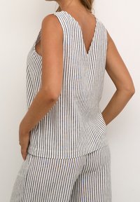 Haut sans manches rayé en blanc, bleu et beige. Dispose d'un dos en V, d'une coupe décontractée et d'une poche sur le côté. Fabriqué en tissu léger.