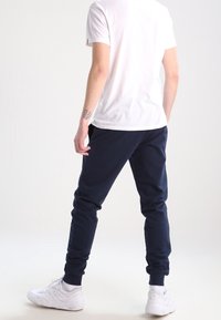 Pantalones deportivos azul marino confeccionados con tela suave, con un corte entallado y puños elásticos, combinados con una camiseta blanca lisa y zapatillas blancas.