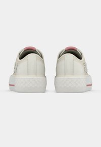 Μπεζ αθλητικά παπούτσια με υφή στη λευκή σόλα, ροζ λεπτομέρειες στη φτέρνα και κλασικό σχεδιασμό με κορδόνια. Ορατές ενισχυμένες ραφές.