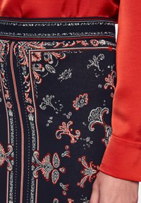 Navy patterned skirt featuring intricate floral designs in red and white. Smooth fabric with a contrasting solid red top section.