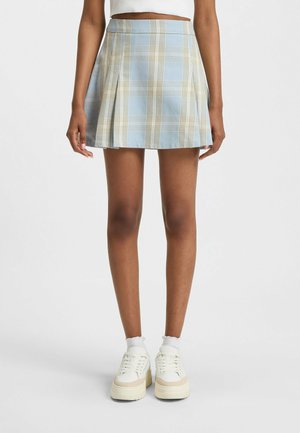 Pleated short skirt in light blue and cream plaid pattern, made of soft fabric. Paired with chunky white sneakers and white ankle socks.