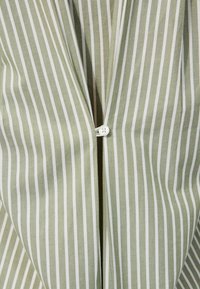 Close-up of green and white vertical striped fabric with a single white button fastened at the center.