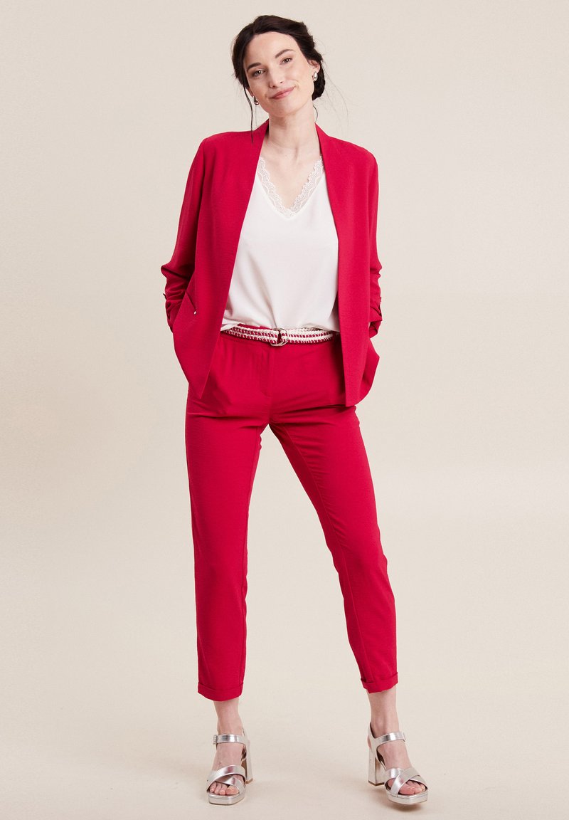 Blazer rosso e pantaloni abbinati con un taglio su misura, abbinati a un top bianco con pizzo. Tacchi a blocco argento completano il look.