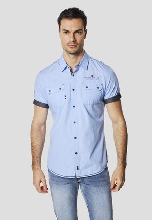 Camicia celeste chiaro con bottoni e maniche corte, due tasche sul petto, bottoni neri e dettagli in denim blu sui polsini. Dettaglio logo sottile sulla parte anteriore.