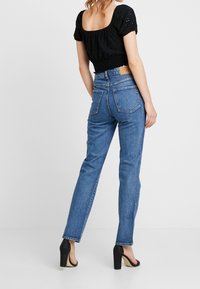 Jean en denim bleu clair taille haute avec jambes droites, présenté de dos, comprenant deux poches arrière et des détails de couture subtils.