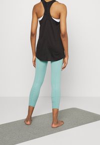 Svart ärmlös träningslinne med justerbar baksida och ljusblå leggings. Leggingsen har en figurnära design och synliga sömmar.