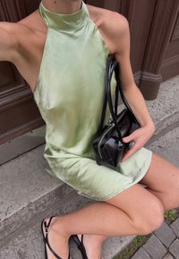 Mintgrön, satin halterneckklänning med hög krage; parat med en liten svart handväska. Bäraren sitter på stensteg och har svarta sandaler på.