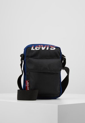 Czarna torba na ramię Levi’s z niebieskimi krawędziami, przednią kieszenią, czerwoną metką z logo Levi’s i regulowanym czarnym paskiem, wyeksponowana na białej powierzchni.
