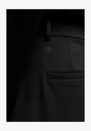 Črne športne hlače z gladko teksturo, z manjšim logotipom in skrito žepom na hrbtni strani. Tkanina se zdi raztegljiva in trpežna.