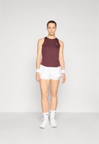 Camiseta deportiva marrón, pantalones cortos blancos, calcetines tobilleros blancos con logo negro y zapatillas blancas. Textura suave, diseño de corte moderno.