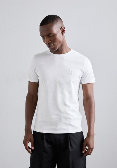 T-shirt blanc à manches courtes en coton, avec un petit logo brodé sur la poitrine. Coupe standard, texture lisse, design à col rond.