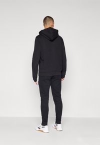 Čierna mikina s kapucňou a zodpovedajúce jogger nohavice vyrobené z mäkkého materiálu, so špicatou prednou vreckou a rebrovanými manžetami, doplnené bielymi športovými topánkami.