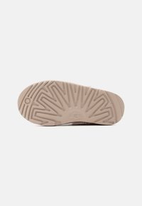 Εσωτερική σόλα παπουτσιού μπεζ με σχεδιασμένο πέλμα και ανάγλυφο λογότυπο UGG στο κέντρο, εμφανιζόμενη σε απλό λευκό φόντο.