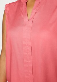 Różowa bezrękawnikowa bluzka z dekoltem w kształcie litery V i koronkowymi detalami na ramionach. Gładki materiał o miękkiej teksturze i luźnym kroju.