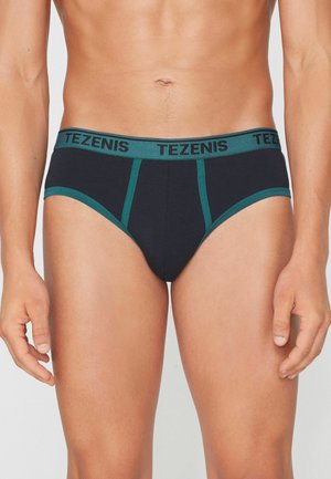 Männlicher Torso trägt schwarze Slips mit grünem Besatz und Bund, gebrandmarkt mit "TEZENIS" in fetten Buchstaben.