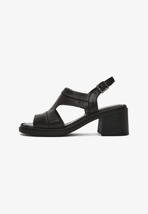 Sandale noire en cuir à bout ouvert avec talon bloc, bride de cheville à boucle et côtés découpés, vue de profil sur fond blanc.