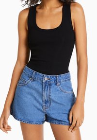Černý žebrovaný top na ramínka s širokými popruhy, spárovaný s modrými denimovými šortkami s vysokým pasem, které mají přední knoflík, kapsy a třepený lem.