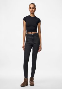 Μαύρο κοντομάνικο μπλουζάκι, ψηλόμεσα σκούρα τζιν και καφέ σουέτ μπότες. Τα τζιν έχουν λεία υφή και εφαρμογή slim.