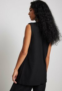 Must mustriga ülikond, mis on valmistatud siledast kangast, omab lõdva istuvust ja peent langevust, ümarat äärist ning ei sisalda nähtavaid dekoreerimisi.