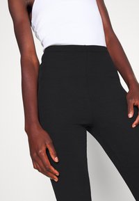 Černé žebrované legíny s vysokým pasem, měkkou texturou a přiléhavým střihem, doplněné bílým tílkem.