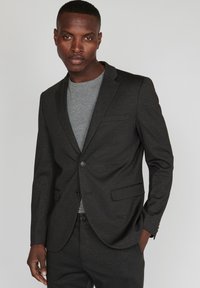 Tumed hall blazer slim fit'i, ühe nupuga sulgemisega, soonikute krae ja kahe eesoleva taskuga. Kantakse heledast hallist T-särgist üle.