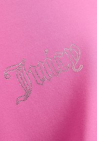 Besedilo v stilu pisave s pergamentom "Juicy", oblikovano z majhnimi srebrnimi kristalčki na svetlo rožnati tkanini.