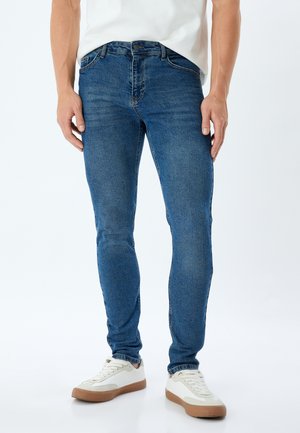 Vaqueros ajustados de mezclilla azul, con cinco bolsillos, una cintura con trabillas para cinturón y una leve textura desgastada en la tela.