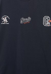 Trois logos blancs et orange sur le thème de Dingo sur un tissu foncé : Dingo dansant, texte « Goofy Country Club » et tête de Dingo dans une lettre G.