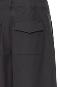Gros plan sur un pantalon en tissu foncé avec une grande poche arrière rectangulaire à rabat pointu.
