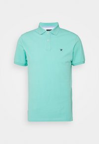 Polo shirt vert clair en coton, avec un col, des manches courtes et un petit logo marine sur la poitrine gauche. Coupe décontractée, texture lisse.