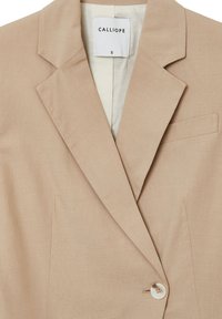 Beiger Blazer mit strukturiertem Design, Reverskragen, einem Knopfverschluss und einer Brusttasche. Das Material weist eine subtile Textur auf.