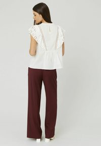 Blouse blanche avec des détails en dentelle sur les épaules, dos en forme de clé, associé à un pantalon large bordeaux. Texture lisse sur les deux vêtements.