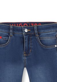 Jeans de mezclilla azul oscuro con un diseño ajustado, costuras naranjas, cierre de botón y bolsillos frontales. Marca HUGO visible en la cintura.