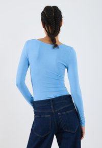 Lys blå langermet topp med et fitted design, med vid udskæring. Kombinert med mørk blå denimjeans, som har klassiske baklommer.