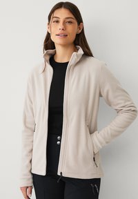 Giacca in pile beige con colletto alto, due tasche laterali e cordini regolabili all'orlo; texture morbida e design leggero.