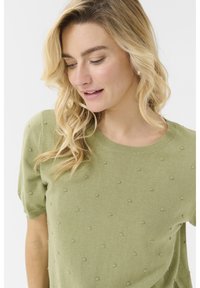 Pulover verde deschis cu mâneci scurte, decolteu rotund și model texturat cu biluțe. Materialul moale din tricot oferă o fixare confortabilă.