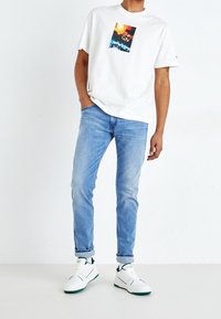 Vit t-shirt med tryck, ljusblå jeans och vita sneakers med gröna accenter. Avslappnad passform och bomullsmaterial.