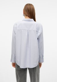 Camicia azzurro chiaro a maniche lunghe con vestibilità rilassata, dettaglio della piega sul retro, polsini con bottoni e una trama di tessuto morbido e liscio.