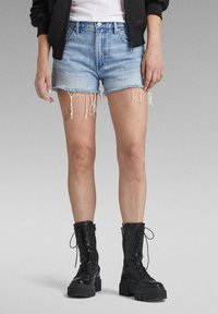 Shorts en denim bleu clair avec des ourlets effilochés, associés à des bottes de combat noires à lacets avec des semelles épaisses et des détails de zip.