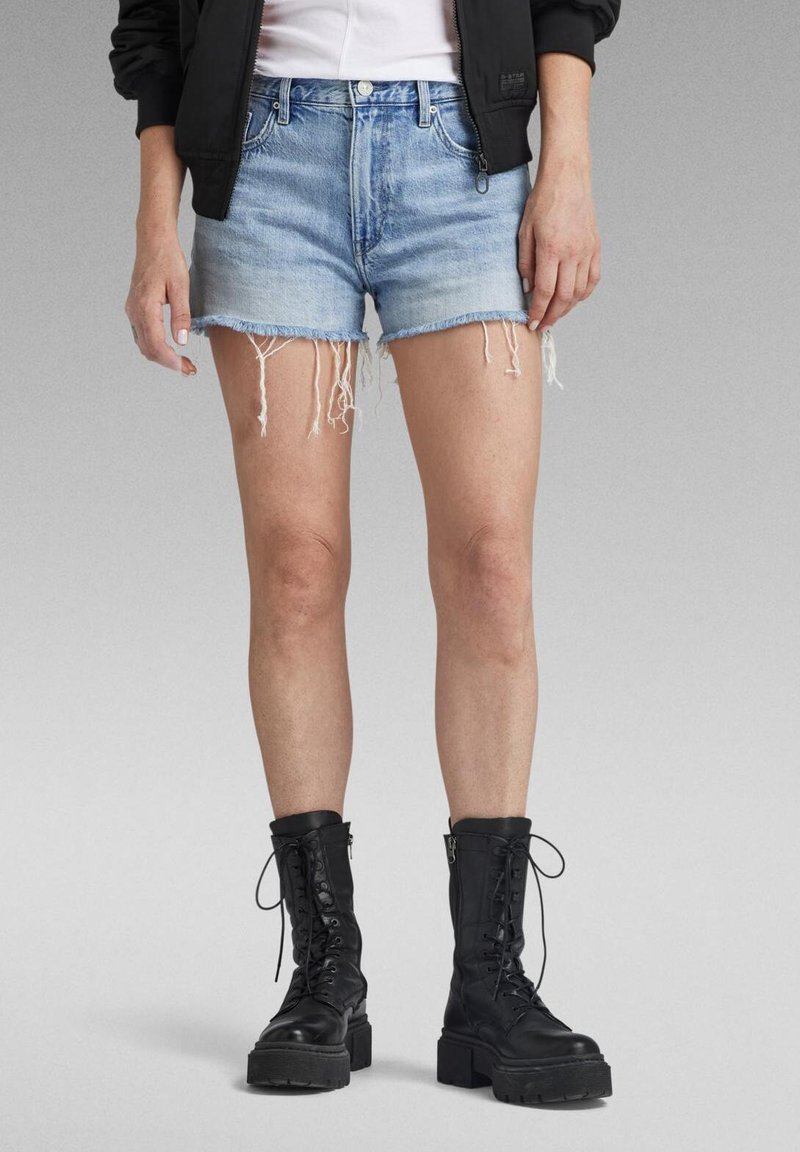 Shorts en denim bleu clair avec des ourlets effilochés, associés à des bottes de combat noires à lacets avec des semelles épaisses et des détails de zip.