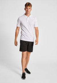Hvid polo skjorte med korte ærmer, kombineret med sorte shorts og sorte sneakers. Simpelt design, ingen mønstre eller iøjnefaldende accenter.
