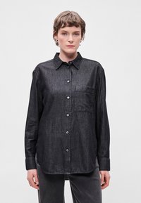 Σκοτεινό τζιν πουκάμισο με γιακά, μακριά μανίκια, τσέπη στο στήθος και μικρά κουμπιά. Το ύφασμα έχει υφή.