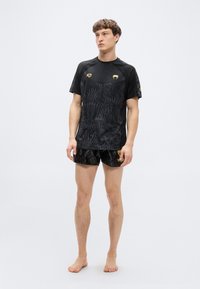 Μαύρο αθλητικό μπλουζάκι με υφασμένο σχέδιο, κίτρινα στοιχεία και μαύρο σορτς με σχέδιο. Ελαφρύ, εφαρμοστό σχέδιο κατάλληλο για αθλητικές δραστηριότητες.