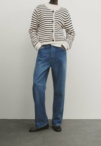 Sweter w paski w kolorze kremowym i granatowym, zapinany z przodu, połączony z luźnymi niebieskimi dżinsami i czarnymi botkami za kostkę.