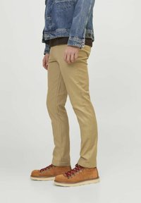 Chino beige con una vestibilità slim, realizzati in tessuto misto cotone. Presentano tasche laterali, dettagli di cucitura discreti e una texture liscia.