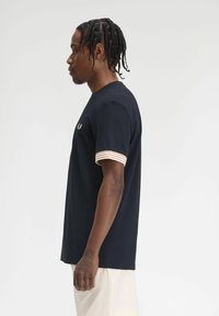 T-shirt in cotone blu navy con maniche a righe beige e bianche, caratterizzato da un piccolo logo ricamato sul petto. Maniche corte e vestibilità rilassata.